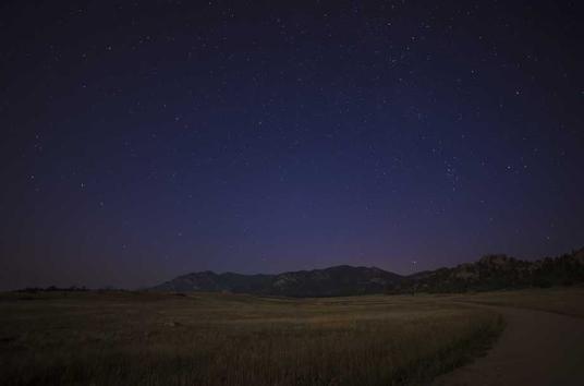 Night landscape, possibly long exposure? Can see stars and dark purple blue sky, with grassy landscape in foreground.